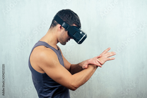 a young handsome man in a virtual reality mask (glasses) looks down and at his hands. the concept of video games and reality