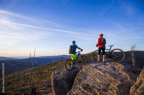 Cycling woman and man riding on bikes at sunset mountains forest landscape. Couple cycling MTB enduro flow trail track. Outdoor sport activity.