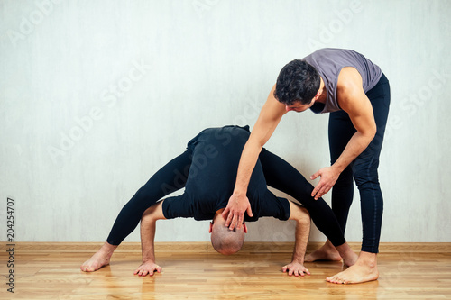 young and athletic man practices yoga and performs asanas together with an instructor in the gym
