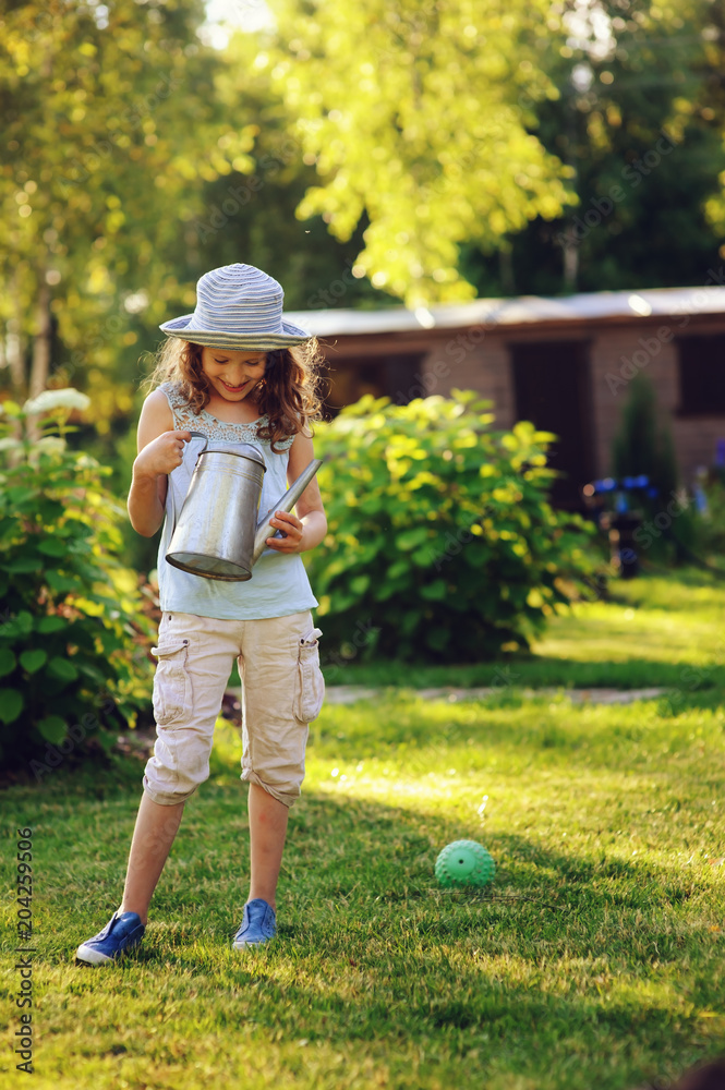 vertical portrait of happy child girl in gardener hat playing with watering can in sunny summer garden vertical portrait of happy child girl in gardener hat playing with watering can in sunny summer garden
