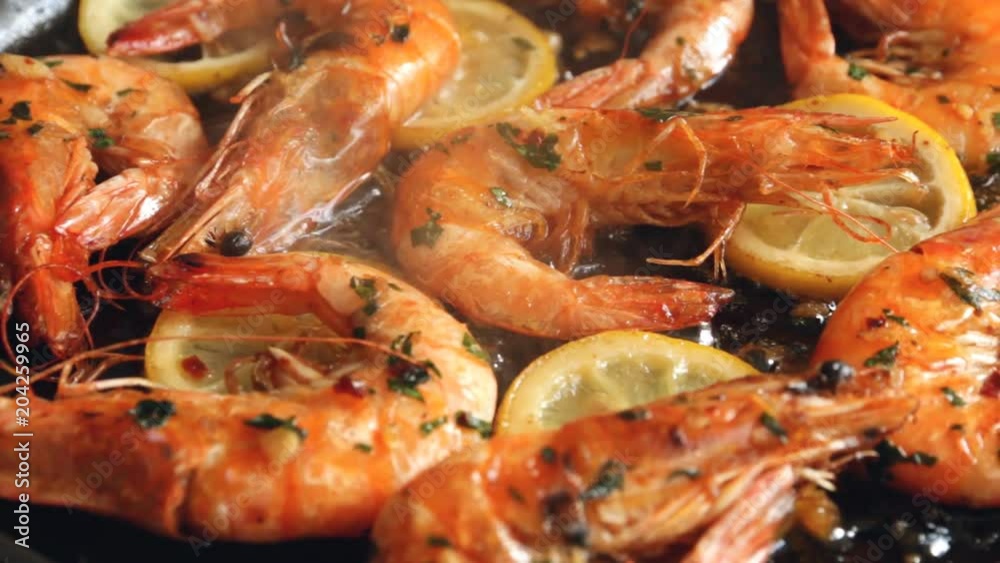 cooking fried roasted shrimps in frying pan with lemon greens parsley garlic