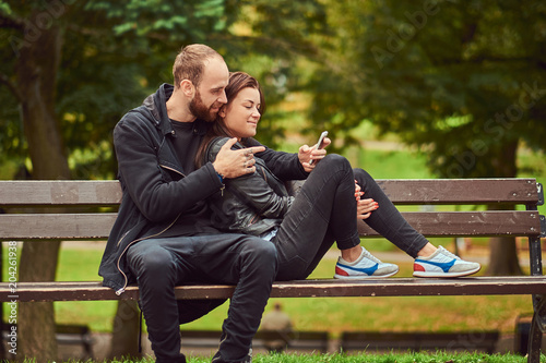 Attractive modern couple sitting on a bench in a park. © Fxquadro