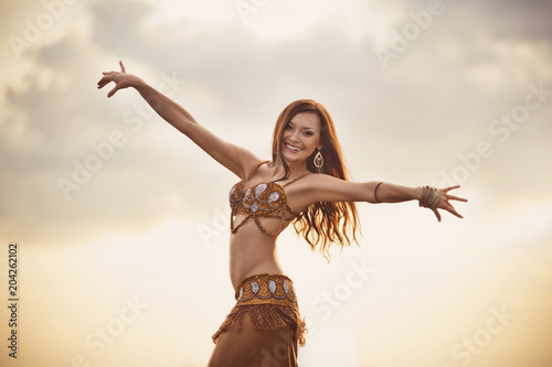 Dancer of bellydance in a gold suit on the background of a canyon. Beautiful nature at sunset. Belly dance. Girl with exotic appearance. Oriental beauty.