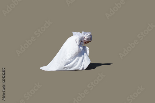 A beautiful woman in white kneeling in prayer, her eyes closed, head bowed and hands clasped