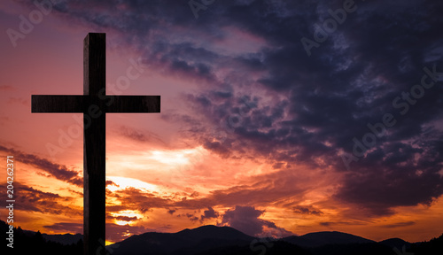 Jesus Christ cross, wooden crucifix. Crucifixion concept on a heavenly background with dramatic light and clouds and colorful orange, purple sky at sunset. Religious Easter, resurrection concept