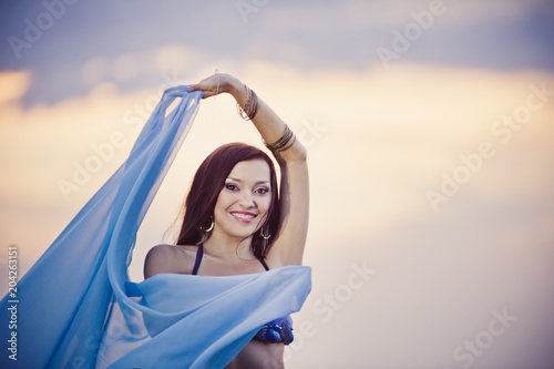 Dancer of bellydance in a blue suit on the beach  against the background of the water. Beautiful nature at sunset. Belly dance. Girl with exotic appearance. Oriental beauty.
