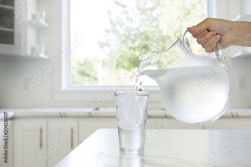 A woman’s hand pouring ice water from a pitcher into a glass.