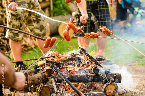 Grilling sausages over a campfire in the forest. Holiday and summer camping in the countryside. Beltaine night in the Czech Republic. May day celebrations. 