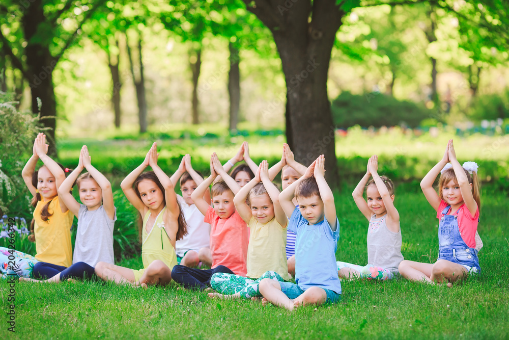 Naklejka premium A large group of children engaged in yoga in the Park sitting on the grass.