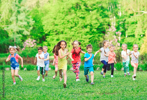 Many different kids, boys and girls running in the park on sunny summer day in casual clothes