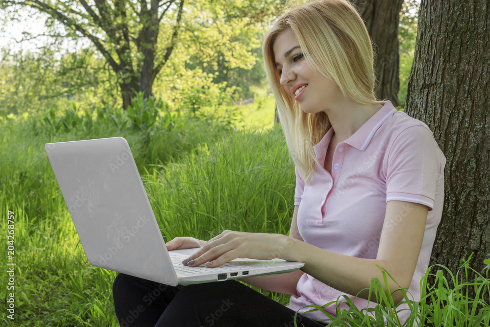Girl, blond, working behind laptop under a tree outdoors Girl, blond, working behind laptop under a tree outdoors
