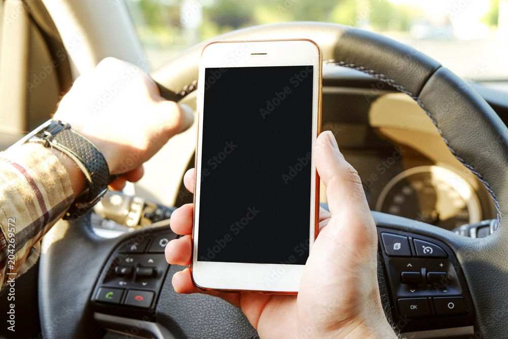 Young man holding blank screen cell phone while driving car. Male