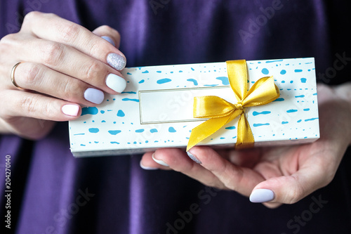 Present box with a gold bow with macaroons inside. Woman holds a box with biscuits.