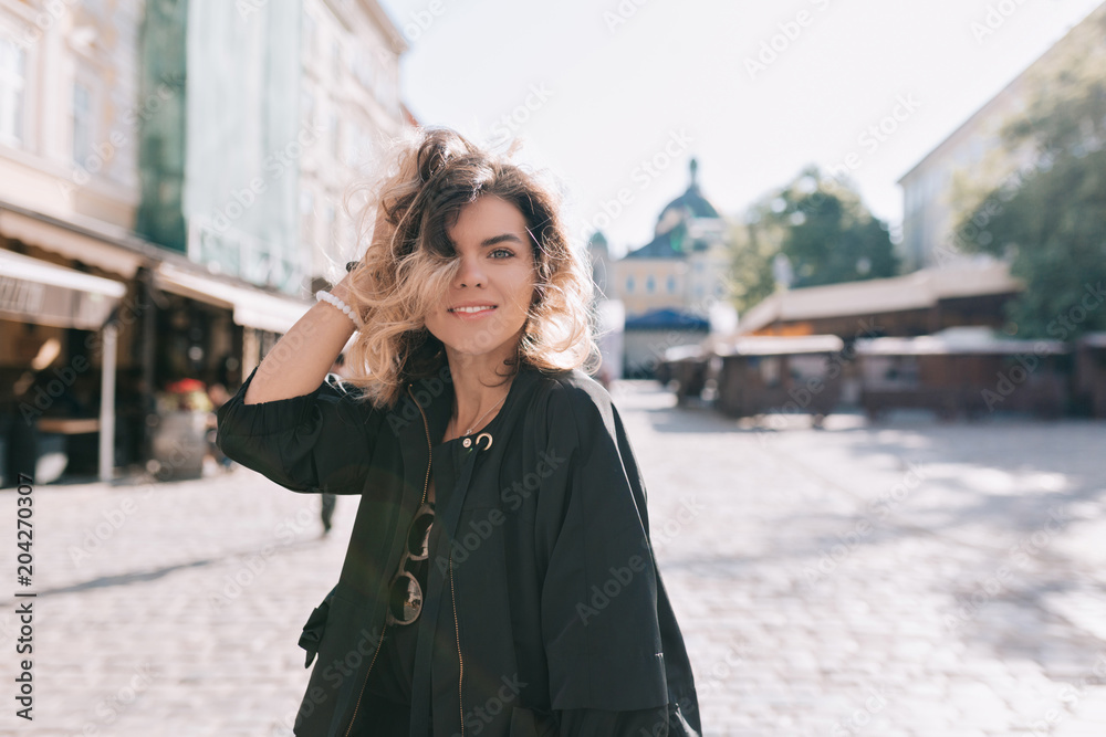 Active stylish happy woman with green eyes and stylish short hairstyle dressed black dress walks down the street in sunny day in the morning, happy student traveling in Europe