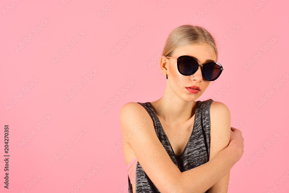 Closeup portrait of blond model with ponytail in melange gray sleeveless blouse wearing big black sunglasses isolated on pink background. Summer eyewear fashion