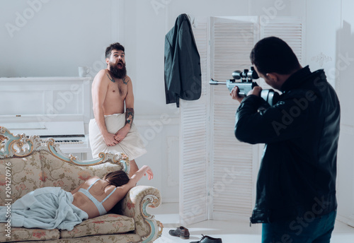 Man at gunpoint of killer. Husband found lovers, killed wife and threatening to bearded lover. Man with beard naked, scared, shocked at gunpoint, interior background. Cheating and jealousy concept. photo