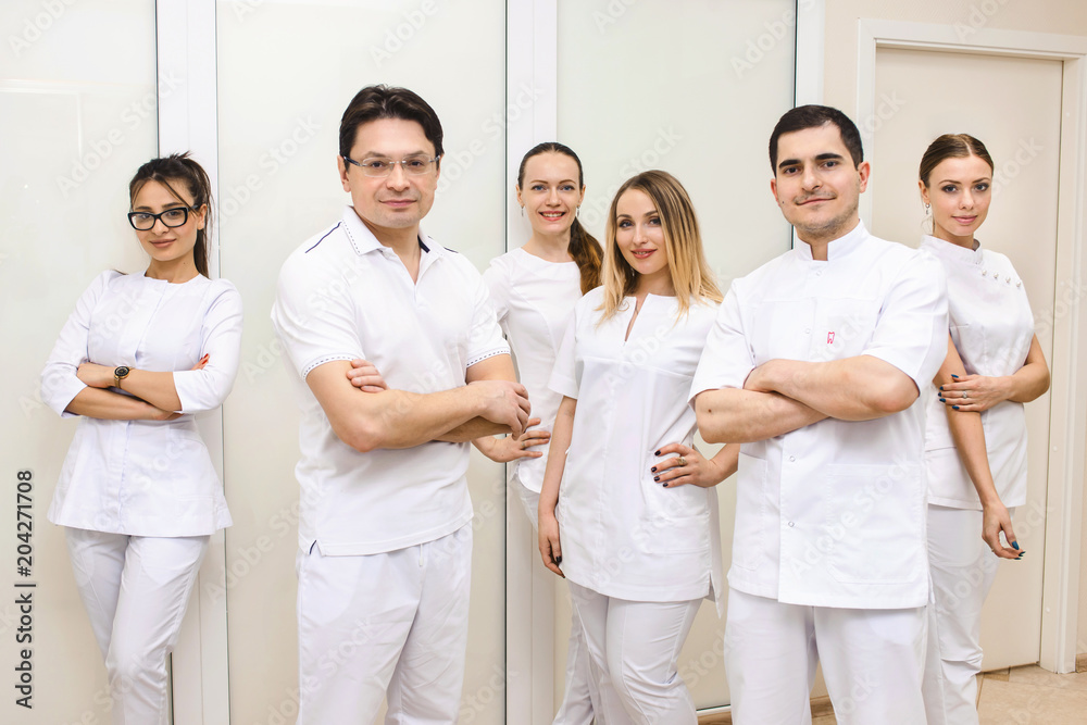 Cheerful group of young dentists and their assistants standing in the dental office and looking at camera and friendly smiling at white background of medical room. Cheerful group of young dentists and their assistants standing in the dental office and looking at camera and friendly smiling at white background of medical room.