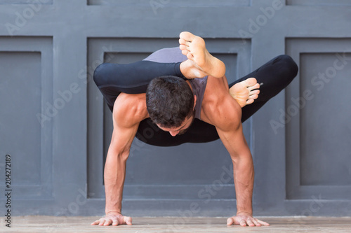 Man doing yoga exercises and practicing handstand balance pose on grey urban background.