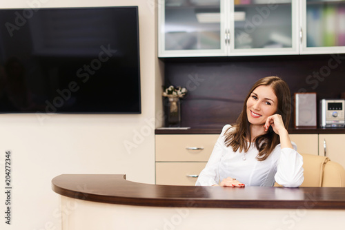 Beautiful female smiling receptionist or secretary at reception in medical clinic or hospital is waiting for patient. Copyspace for text. photo