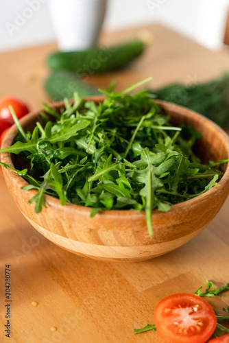 Wooden Bowl of fresh green  natural arugula with red tomatoes on a wooden background