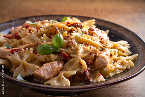 Pasta with chicken, sun dried tomatoes and basil in creamy mozzarella sauce in bowl on wooden table. horizontal