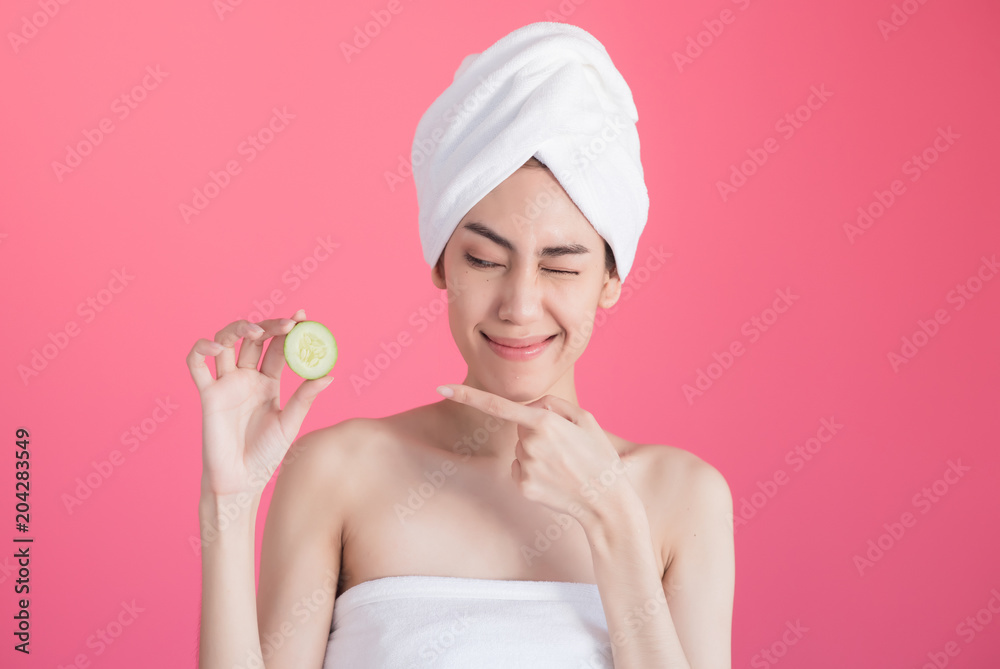 beautiful asia woman with towel on head with perfect clean skin smiling holding cucumber slices over pink background. Beauty cosmetology and spa. beautiful asia woman with towel on head with perfect clean skin smiling holding cucumber slices over pink background. Beauty cosmetology and spa.