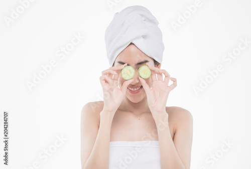 beautiful asia woman with towel on head with perfect clean skin smiling holding cucumber slices over white background. Beauty cosmetology and spa.