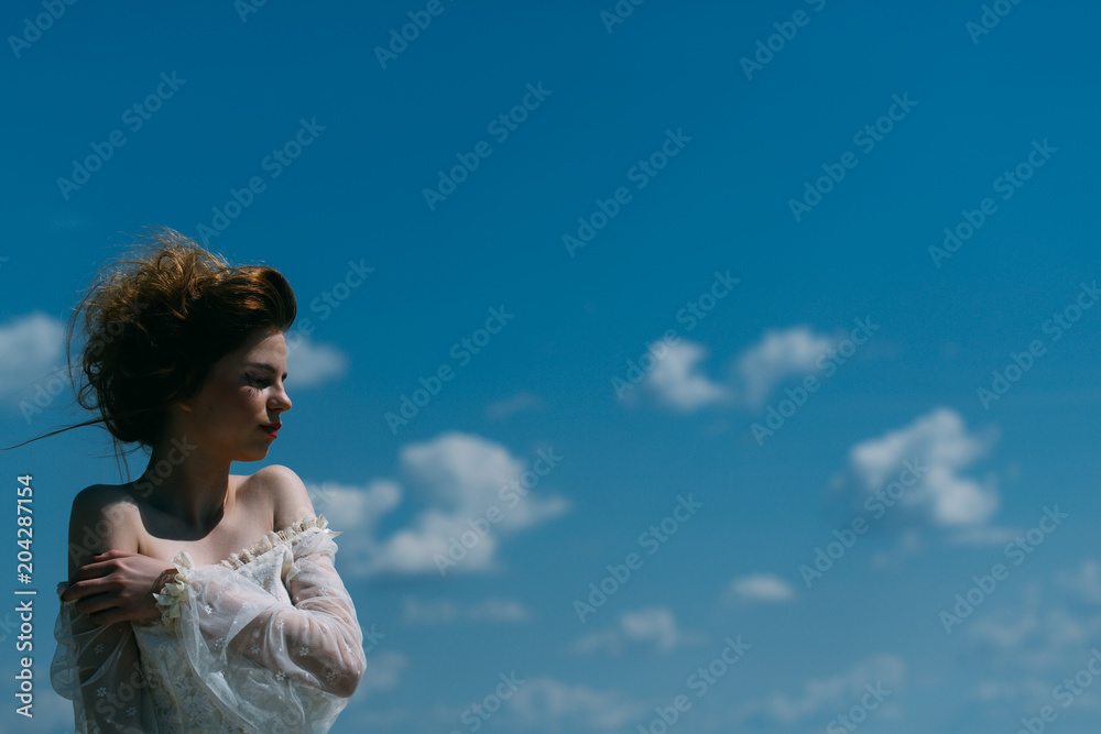 Makeup on young face. Beauty and fashion look in vintage style. Pretty girl in white wedding dress and retro hairstyle. Fashion woman model pose outdoor. Girl on sunny blue sky background in summer. Makeup on young face. Beauty and fashion look in vintage style. Pretty girl in white wedding dress and retro hairstyle. Fashion woman model pose outdoor. Girl on sunny blue sky background in summer.