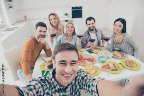 Handsome, attractive, stylish man making self portrait with best friends on blurred background sitting at the table holding glasses with red wine, celebrating holiday indoor