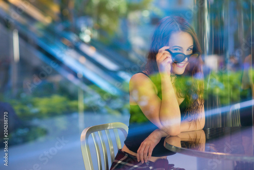 Young woman looking over sunglasses behind blue and green reflected glass