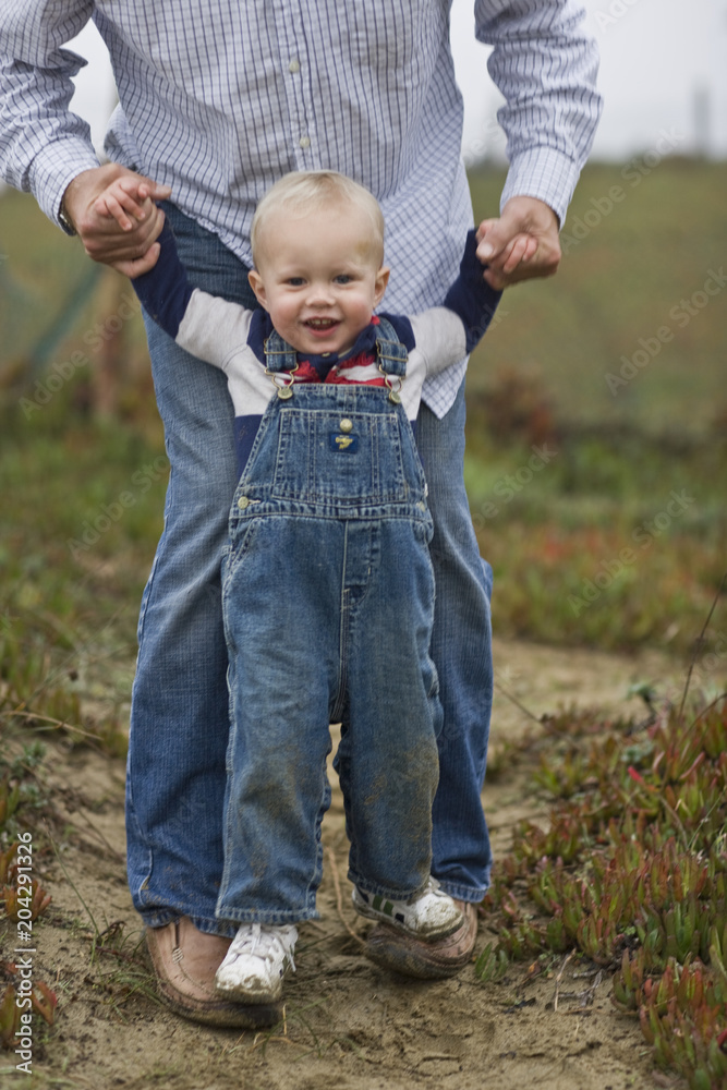 Toddler boy walking on father's feet outdoors Toddler boy walking on father's feet outdoors