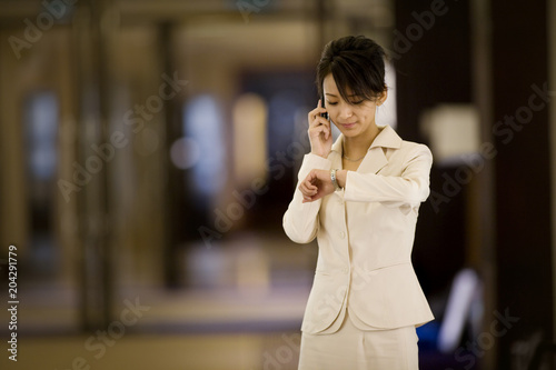 Young adult business woman checking her watch while using a cellphone in an office.