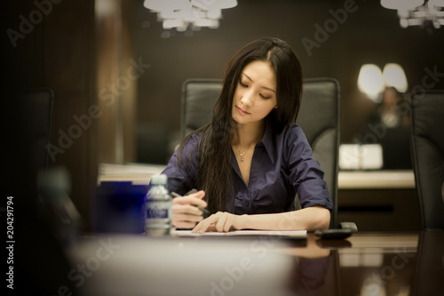 Young adult business woman taking notes in a boardroom.