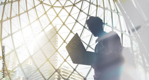 Silhouette of young intelligent man managing a computer in modern office environment with copy space for your text message or promotional content. photo