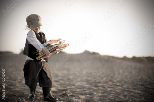 Little boy in victorian era clothing carrying books along beach photo