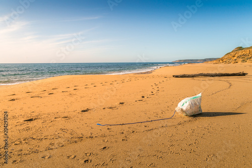 Footprints and garbage on a beach in a sunny day