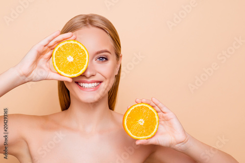 Pretty charming joyful attractive cheerful funny comic positive nude natural pure girl having two pieces of orange, closing one eye, isolated on beige background with copy space for advertisement photo