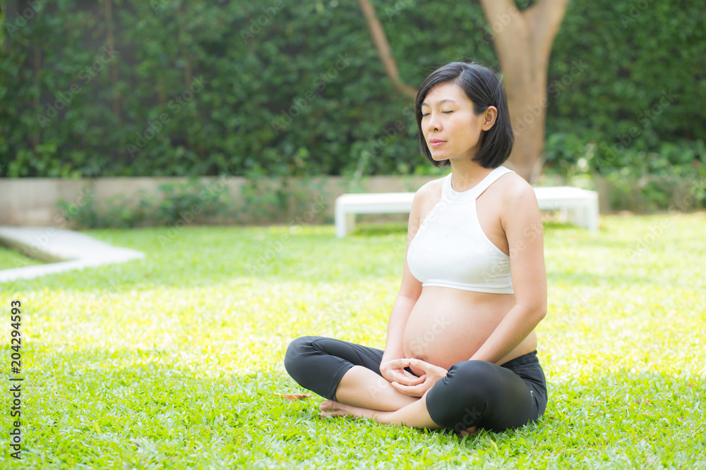 Beautiful pregnant asian young woman relax in the park, girl with belly sitting with crossed leg on grass and yoga exercise for wellness, copy space. Beautiful pregnant asian young woman relax in the park, girl with belly sitting with crossed leg on grass and yoga exercise for wellness, copy space.