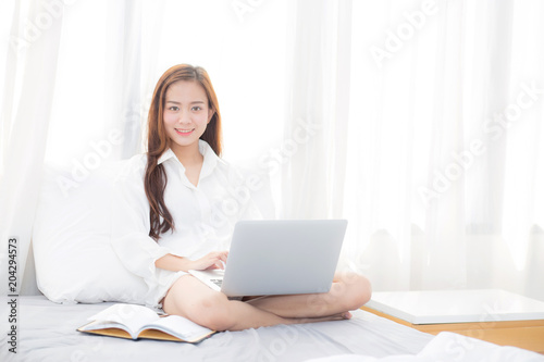 Beautiful asian young woman setting on bed using laptop computer and notebook at bedroom for leisure and relax  freelance with girl working at bedroom with note  communication and lifestyle concept.