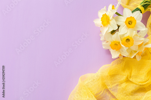Fototapeta Naklejka Na Ścianę i Meble -  Daffodil bouquet with yellow textile decoration on violet pastel background with copy space.