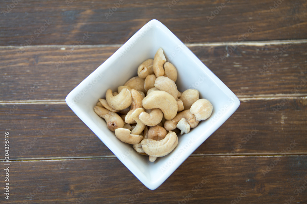 cashew nuts inside white bowl on a wooden table viewed from above cashew nuts inside white bowl on a wooden table viewed from above