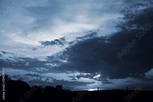 Dramatic mysterious dark blue sky with clouds, black horizon with silhouettes of a city, sunset