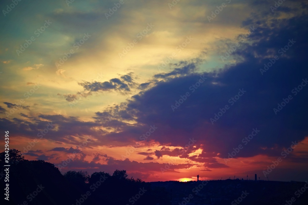 Dark colorful dramatic sky with clouds, red sunset over black horizon with silhouettes of a city