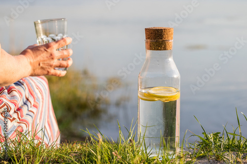 A bottle of water with lemon and a glass. A woman drinking water from the lake.