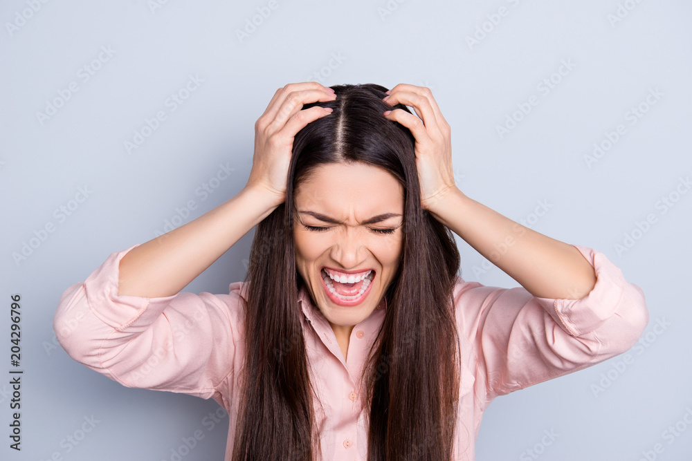 Portrait of mad crazy woman with violent irritated reaction, shouting with close eyes, grimace, tired from routine isolated on grey background, holding two hands on head, out of herself Portrait of mad crazy woman with violent irritated reaction, shouting with close eyes, grimace, tired from routine isolated on grey background, holding two hands on head, out of herself