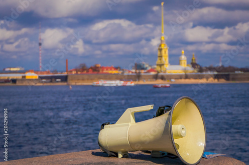 Close up of white megaphone at outsdoors with scenic river view of the Peter and Paul Fortress in the horizont in Saint Petersburg photo