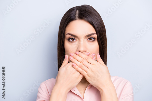 I can't speak! Portrait of pretty charming brunette woman closing her mouth with two crossed palms isolated on grey background, looking at camera