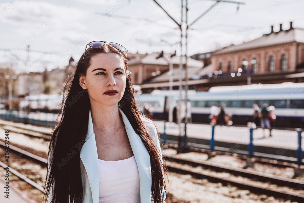 A serious woman returns home from school at work, awaits and looks out for the train. A potrait of a woman dressed in a blue jacket and sunglasses on the sun.