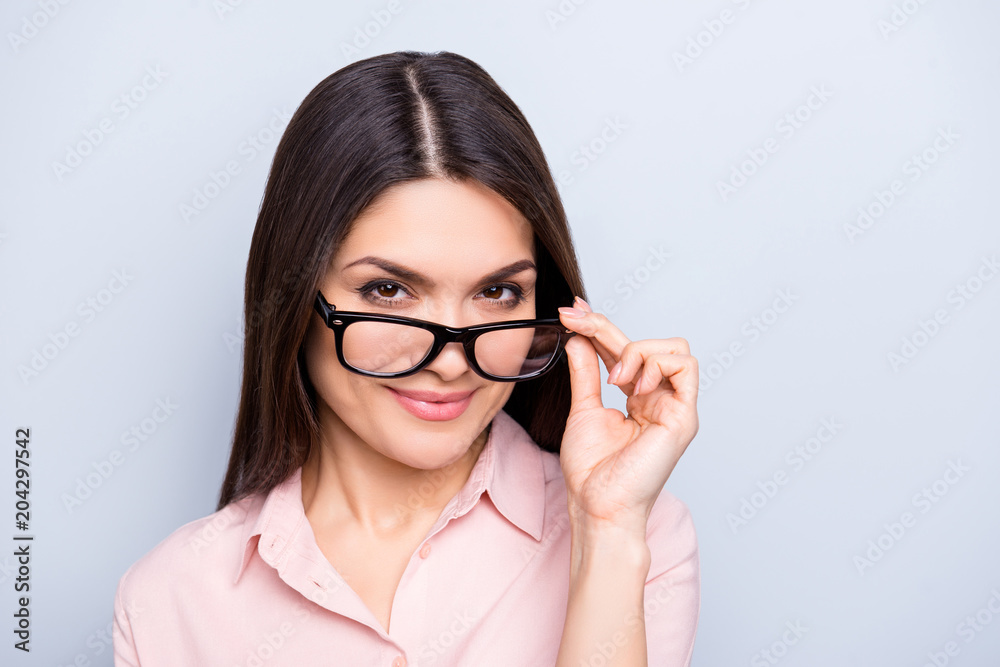 Portrait of clever charming brunette cute pretty woman holding eyelet of glasses on her face, looking out spectacles, isolated on grey background Portrait of clever charming brunette cute pretty woman holding eyelet of glasses on her face, looking out spectacles, isolated on grey background