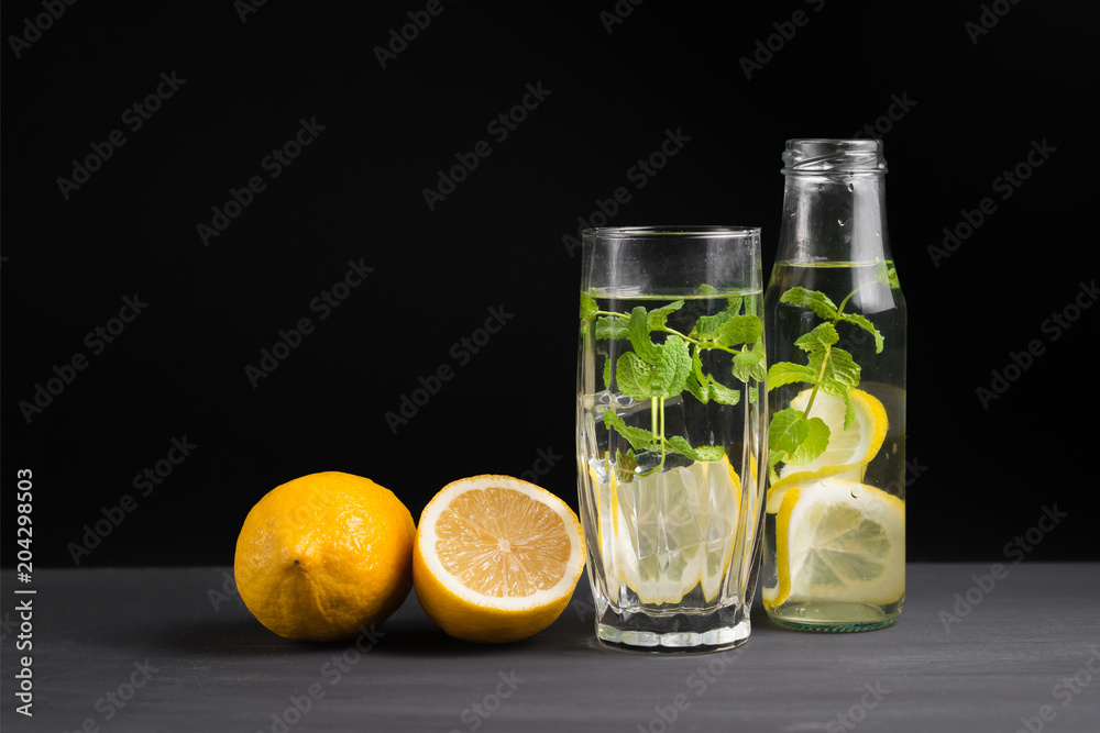Fototapeta premium The concept of holidays and parties, food and drinks. Cold alcoholic cocktail mojito, lemonade with lemon, mint and ice in a glass and a bottle on a black background. Copy background space